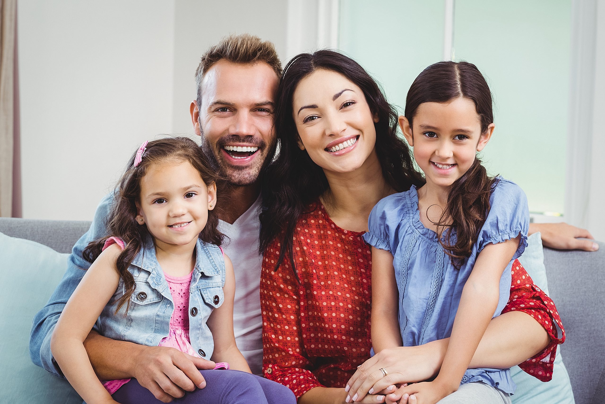 Portrait,Of,Cheerful,Parents,Sitting,With,Daughters,On,Sofa,At Family Portrait